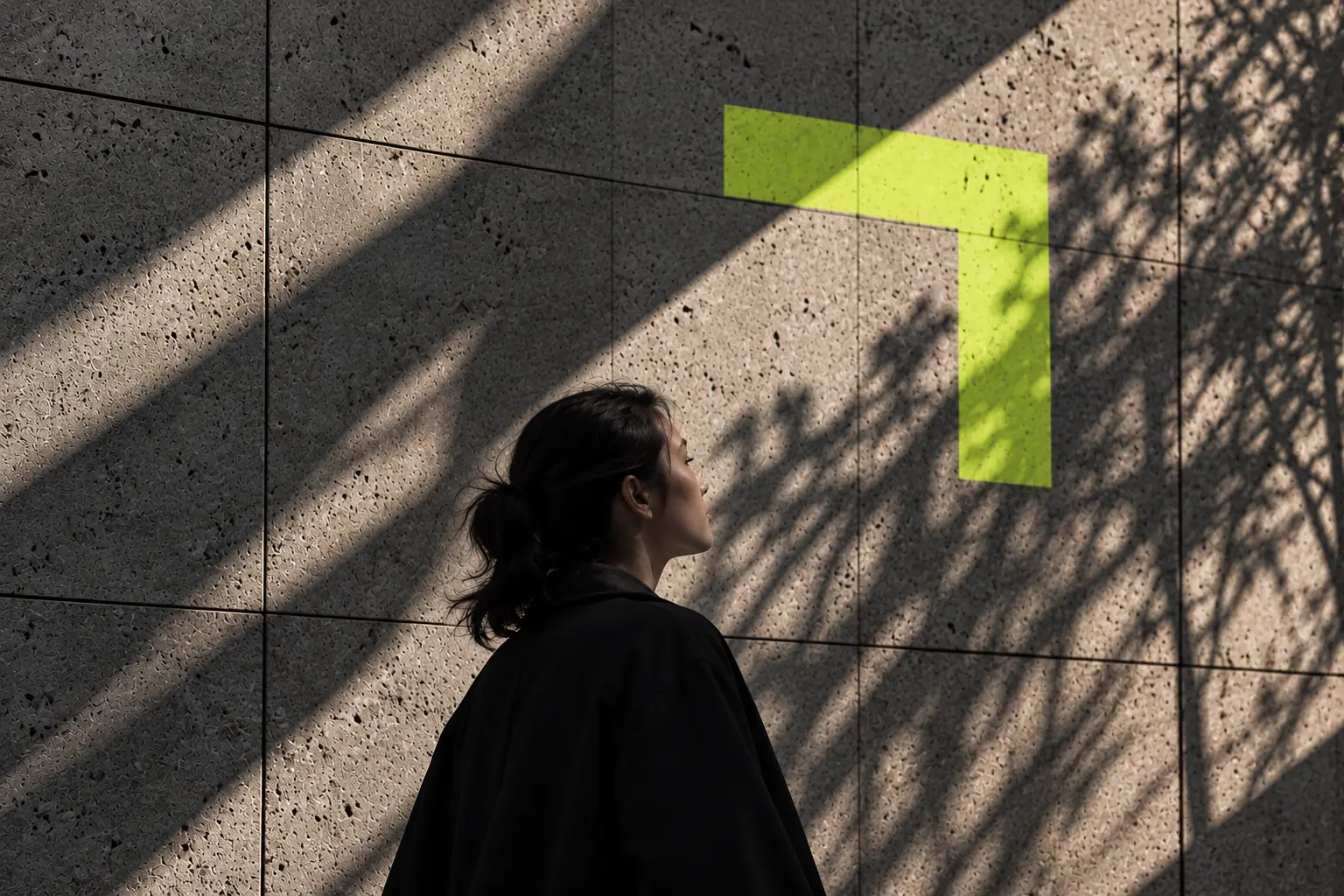 Mulher diante de uma parede de concreto com luz e sombras